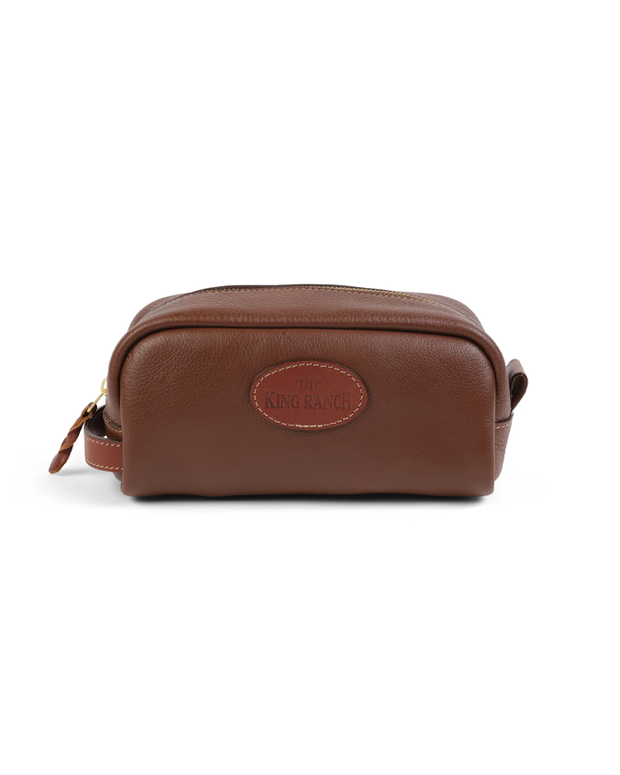 A brown leather toiletry bag with a prominent ‘KING RANCH’ embossed logo on the front, featuring a zipper closure with a leather pull tab, set against a white background.