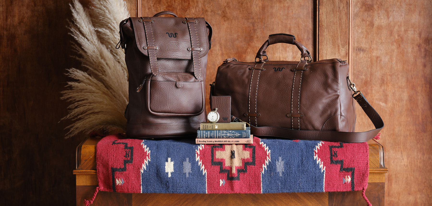 King Ranch's brown leather backpack and brown leather duffle bag are on the blue and red colored blanket.