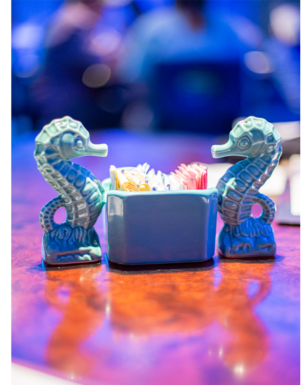 Two, ceramic blue seahorses on each end of a sugar packet holder on a restaurant table.