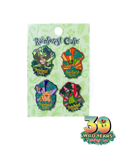 A set of four colorful enamel pins from Rainforest Cafe, each featuring a different animal character. The characters include a green crocodile, a brown jaguar, a green tree frog, & a brown gorilla.  all with the ‘Rainforest Cafe’ logo. These pins are displayed on a decorative card with jungle-themed graphics and a ‘30 Wild Years!’ celebration logo with tree frog sticking out the 0.