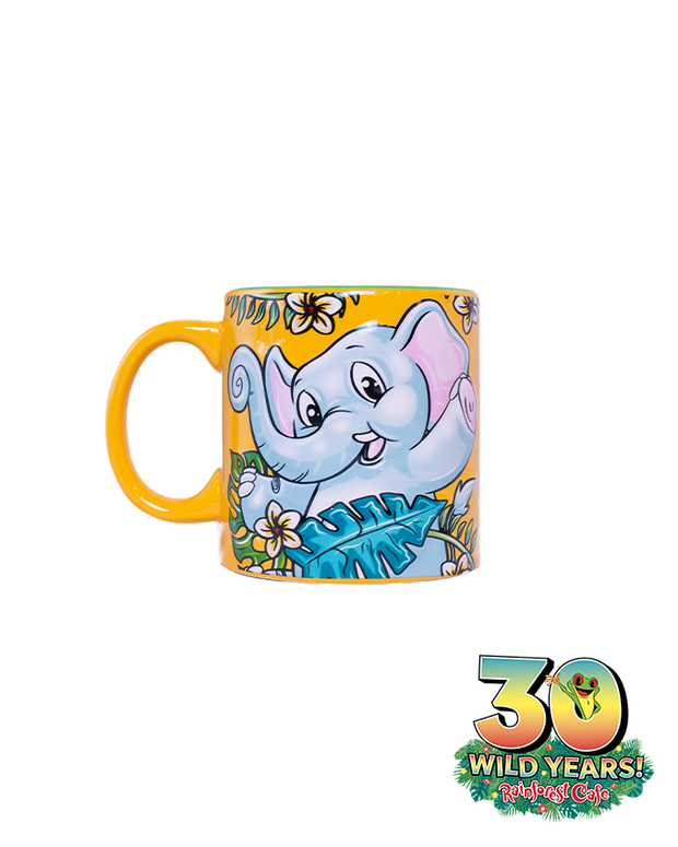 A colorful ceramic mug with a playful illustration of a smiling elephant surrounded by tropical foliage, and a bright yellow handle, commemorating the 30 wild years of Rainforest Cafe. The mug features an emblem celebrating ‘30 WILD YEARS!’ of Rainforest Cafe.