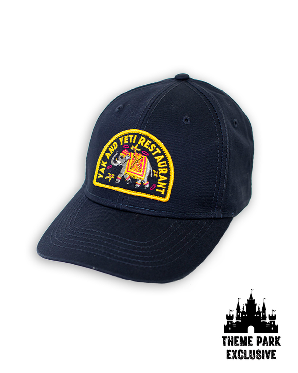 A navy-blue cap with a semi-circle embroidered design reading "YAK AND YETI RESTAURANT" with a decorated elephant in the center. The background is plain white with a Disney Castle logo at the bottom reading "THEME PARK EXCLUSIVE".