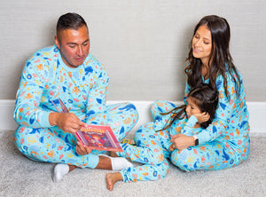 Family of dad, mom, and a daughter sitting on the floor wearing aquamarine blue matching pajamas with sea-inspired print and reading a book. 