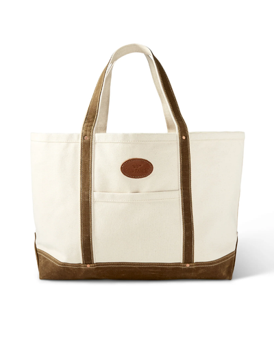 A cream-colored canvas tote bag with contrasting brown leather handles and base, adorned with a small leather logo patch on the front pocket, exuding a simple yet sophisticated style.