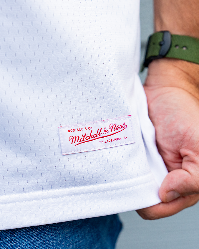 Close-up of a white Mitchell & Ness basketball jersey, featuring a stitched label that reads "Nostalgia Co. Mitchell & Ness, Philadelphia, PA."