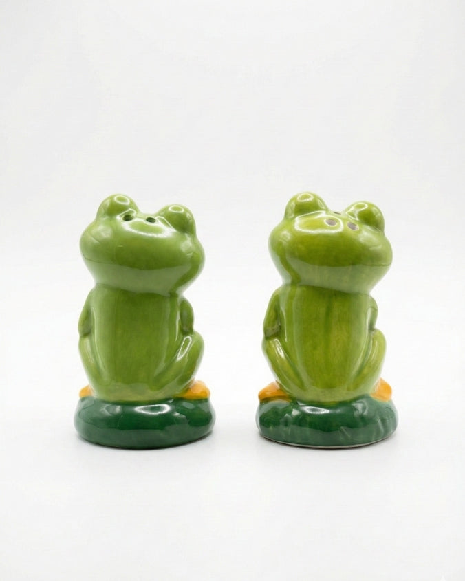 Two green frog-shaped salt and pepper shakers on a white background