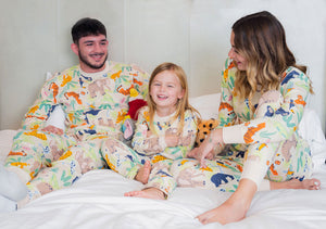 Dad, mom, and daughter are sitting on the bead laughing, all wearing light color-matching pajamas with animal prints. 
