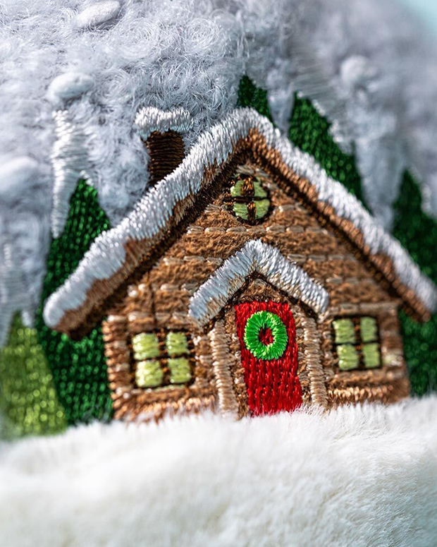 Embroidered design of a snowy cabin with a red door and green windows.