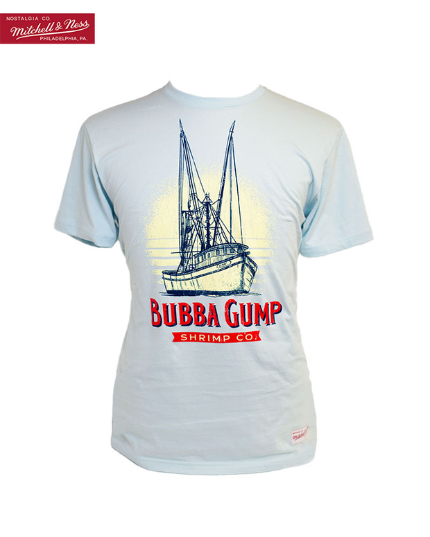 Light blue crew neck short sleeve tee, fitted on the mannequin. It has boat graphics with navy blue shrimp boat outlines and the large white sun setting on the background of the graphics. At the bottom of the shrimp boat is wording in red, "Bubba Gump" and below that in the red ribbon, "shrimp co." Top left maroon tag that reads "Nostalgia Co. Mitchell & Ness Philadelphia, PA."
