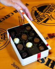 Hand holding a box of chocolates with a brand logo in the background