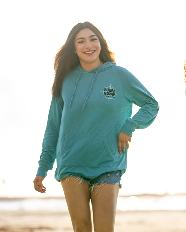 girl walking on beach wearing denim shorts and blue hoodie with drawstrings and a kangaroo pocket. Left check reads "bubba Gump Shrimp co."