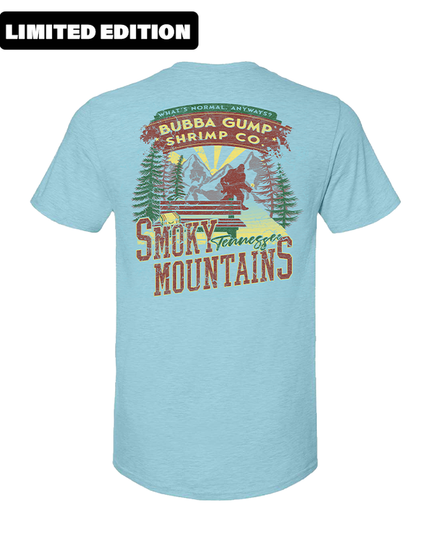 Blue t-shirt with a graphic print on the back. The print features a vintage-style design with the text “Bubba Gump Shrimp Co.” at the top in yellow, followed by an image of a mountain landscape with trees and a setting sun. Below the landscape, “Smoky Mountains” is written in large dark red  letters, and beneath that, in smaller white text, it reads “Tennessee”. The top right corner of the print has a red banner with white text stating 'LIMITED EDITION'.
