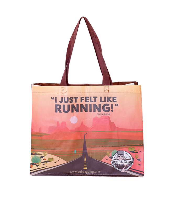 A tote bag with a printed design featuring a quote, ‘I JUST FELT LIKE RUNNING,’ from the movie Forrest Gump. Below the quote is an illustration of Forrest Gump running on a road that stretches across a landscape with greenery and hills in the background. The bottom of the bag displays the Bubba Gump Shrimp Co. logo along with their website address, www.bubbagump.com.