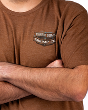 A person wearing a brown t-shirt with a ‘BUBBA GUMP SHRIMP CO.’ logo, standing with arms crossed.
