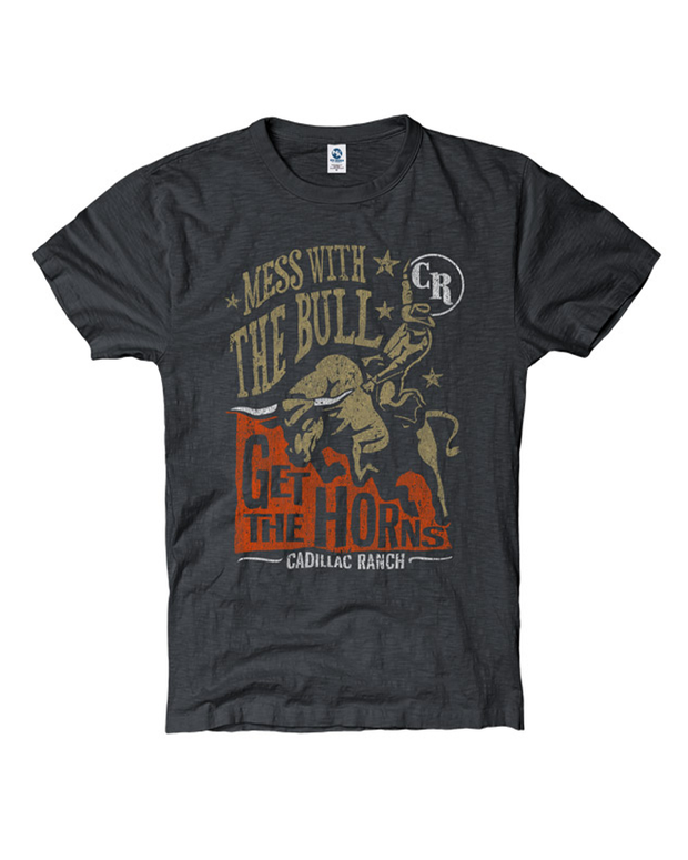The image features a black t-shirt with a graphic design that includes the phrase “Mess with the Bull” in a semi-circle at the top. Below this is an illustration of a bull in motion, appearing to buck or jump. The text “Get The Horns” is displayed prominently beneath the bull. At the bottom of the design, there is another line of text that reads “Cadillac Ranch.” The design has a distressed look, giving it a vintage feel, and includes decorative stars and a brand logo with “CR” initials next to the bull. 