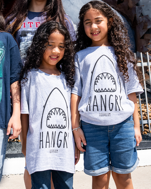 boy and girl wearing matching Grey tee with shark face showing the teeth. Under it, reads "Hangry".