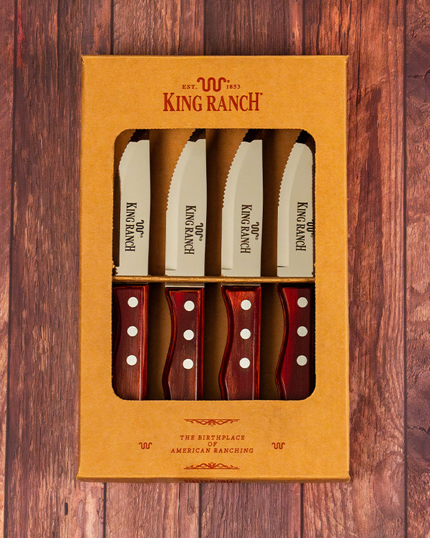 Brown box that contains 4 King Ranch branded steak knives in front of wood background.