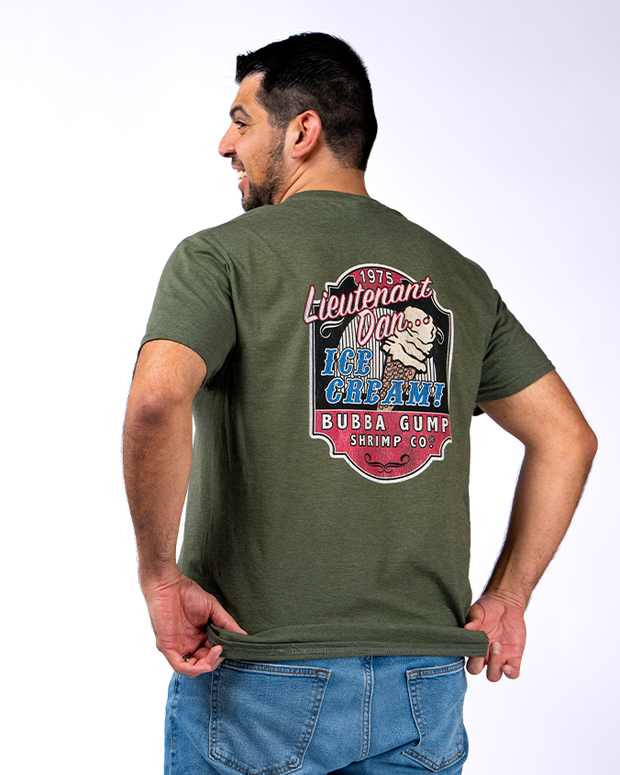 A person wearing a green t-shirt with a colorful print on the back, featuring text and illustrations related to ‘Lieutenant Dan’s Ice Cream’ and ‘Bubba Gump Shrimp Co.’, paired with blue jeans, standing against a white background.