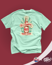 Bubba Gump and Dr. Pepper collaboration.  mint green t-shirt with a vintage Dr. Pepper logo in the center. The logo features a off white banner with “Dr. Pepper” written in red,  and the year “1975” below in off white. Above the banner, “19” and “75” are separated by a glass bottle of Dr. Pepper. Below, there is an additional inscription that reads “BUBBA GUMP SHRIMP COMPANY.” The t-shirt is displayed against a plain maroon background.