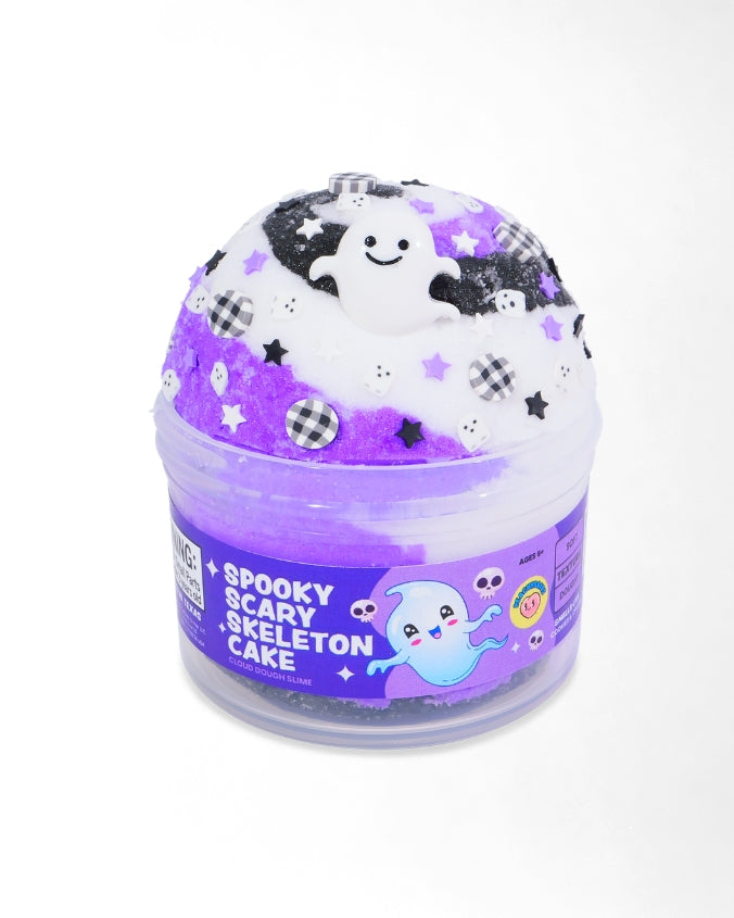 A Halloween-themed slime container labeled 'Spooky Scary Skeleton Cake' on a white background. The container is clear plastic with a purple label featuring a cartoon ghost.