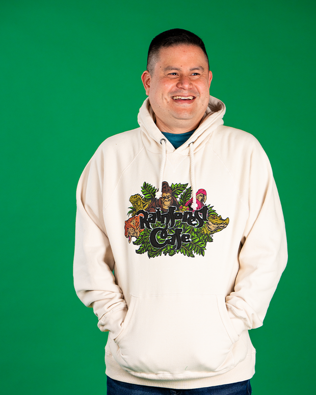 male model in front of green background wearing hoodie. he is smiling, looking to the side with his hands in hoodies kangaroo pouch. 