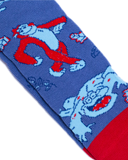 A close-up view of a blue sock with red accents, featuring knitted designs of an oragutang in red and white, and a crocodile in white and light blue.