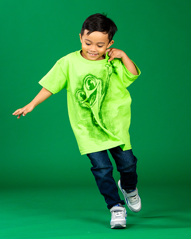 boy model running on green backdrop wearing cha cha tee and denim pants.