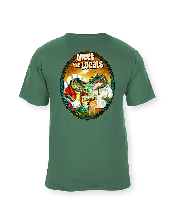 A green t-shirt with a vibrant circular design on the back, featuring cartoon-style illustrations of an alligator and a bird among tropical plants. The text ‘Meet the Locals’ is arched above, and ‘Rainforest Cafe’ is written below the design.