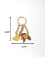 A gold-tone keychain with a banana charm, a monkey charm, and a red script charm, shown with dimension arrows and labels indicating a height of 3 1/4 inches and a width of 2 1/4 inches on a white background.
