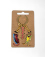 A novelty keychain on a brown cardboard hanger card. The keychain has a gold-tone split ring and chain with three charms: a blue and red striped 'Rolling Stone' magazine cover, a pink rhinestone 'Rolling' text charm, and a green and yellow frog charm wearing a small black top hat.
