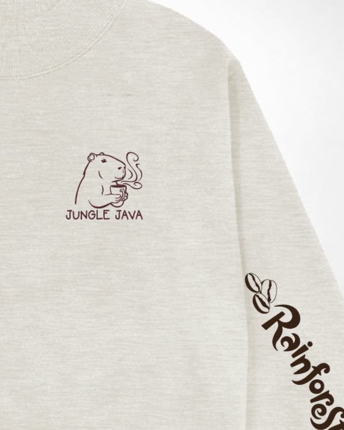 Close-up of a light heather gray sweatshirt showing the chest graphic with a capybara holding a coffee cup and the text 'JUNGLE JAVA', plus a dark script logo on the sleeve.