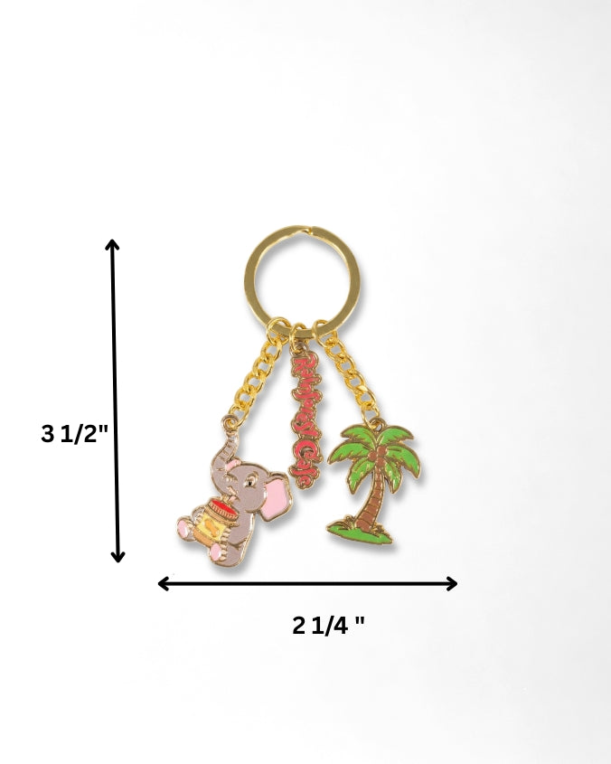 A gold-tone keychain with three dangling charms: a pink elephant holding a yellow pot, a red beaded tassel, and a green palm tree, shown on a white background with measurement arrows and labels indicating 3 1/2 inches tall by 2 1/4 inches wide.