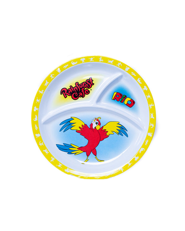 A colorful plastic plate with three compartments, featuring branding and imagery related to the Rainforest Cafe. The main compartment shows a vibrant red parrot with yellow wings spread, set against a light blue background. Above the parrot, the words ‘Rainforest Cafe’ are written in a playful, multicolored font with a yellow outline. The top left compartment has the word ‘RIO’ in bold red letters with a blue outline on a white background. 