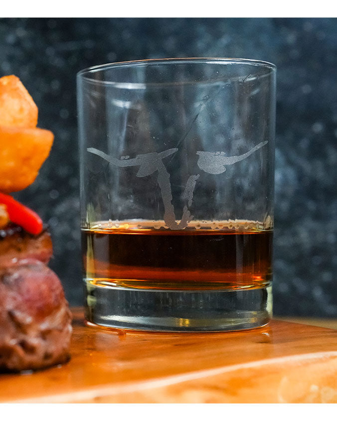 Saltgrass Whiskey Glass with one quarter of it filled, set on top of a wood cutting board., Saltgrass Longhorn etched onto whiskey glass