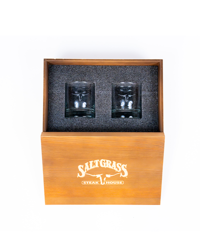 A wooden box with the ‘Saltgrass Steak House’ logo engraved on the front, containing two whiskey glasses cushioned in black foam, set against a white background.