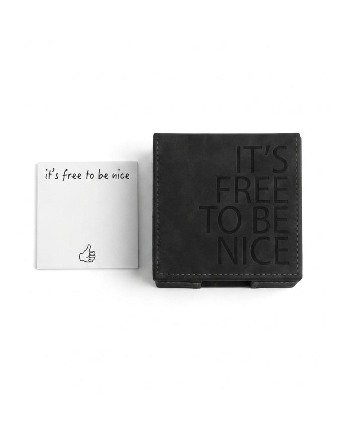 A black textured leather card holder with the embossed text 'IT'S FREE TO BE NICE' next to a white square card printed with 'it's free to be nice' and a thumbs-up icon, on a clean white background.
