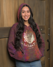 A person stands in front of a wooden door, wearing a colorful tie-dye hoodie featuring a design of Buddha and the text ‘Dwell On Positive Thoughts’, underneath that, reads 'YAK & YETI'. The hoodie displays a vibrant mix of purple, red, and orange hues. The individual’s long, dark hair flows past their shoulders.