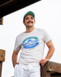 A person stands confidently on a wooden structure, wearing a white shirt with a blue "Bubba Gump Shrimp Co." logo and white shorts.
