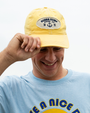 A person wearing a yellow "Bubba Gump Shrimp Co." cap and a light blue shirt with "Have a Nice Day" printed on it.