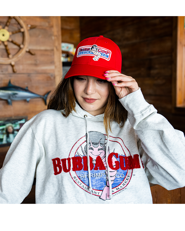 girl wearing red bubba gump cap and Oatmeal colored hoodie with Bubba Gump logo. The logo is a distressed style and the word "bubba gump" is a red applique.