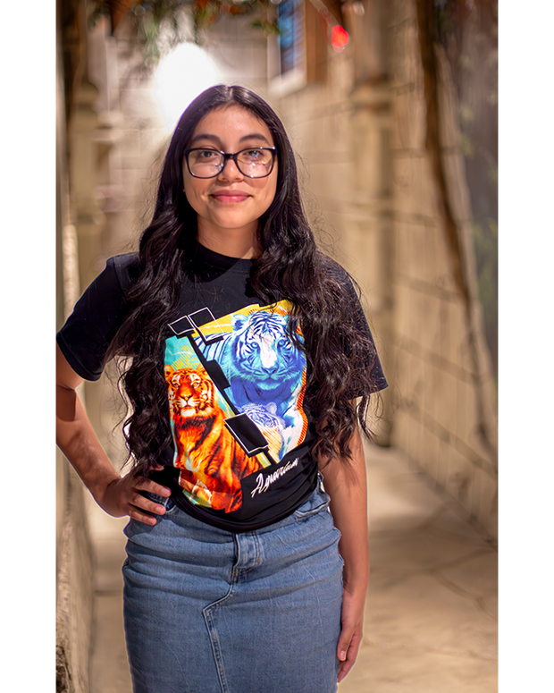 Girl wearing Youth Short Sleeve Tee Shirt black with colorful graphics of Bengal tiger. She is standing in a hall made of stones and greenery on top.
