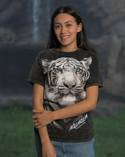 A person wearing a dark-colored t-shirt featuring a large, detailed print of a white tiger’s face with blue eyes. Below the tiger’s face, there is text that reads ‘AQUARIUM HOUSTON.’ The person stands in front of a blurred outdoor background.