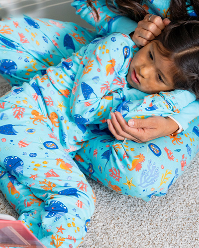 Daughter resting head on mother's lap while wearing Under the Sea PJ set and there is red "Free Shipping" tag in corner.