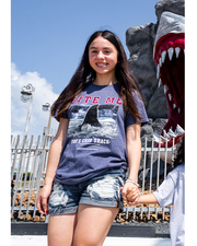 female model wearing denim shorts and Grey tee with "Bite Me" and picture of shark fin coming up from water underneath it.