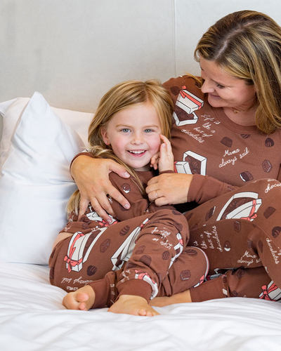 Mom and daughter wearing the brown Box of Chocolates pajama set that has a chocolates pattern with words "Mama always said" and "Life is like a box of chocolates" in white cursive.