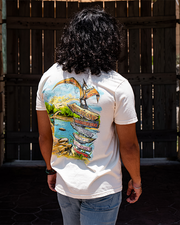 back of male model showing back of shirt. Back graphic deisgn of prehistoric times. A brachiosaurus is crossing a river and behind it are trees and the sun within the sky. Towards the front is a Pterodactyl on top of sign post with different dinosaur names.