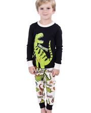 A child in a playful black and white dinosaur-themed pajama set, with a large green dinosaur print on the top and various smaller dinosaur prints on the pants, stands against a white background. The word ‘DINOSNORE’ is visible, adding a fun twist to the bedtime attire.