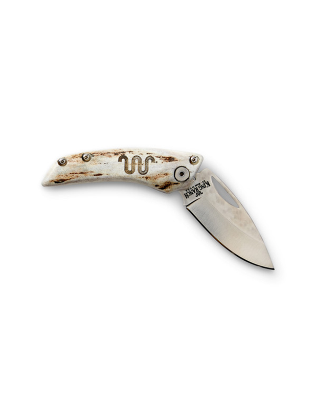A folding knife with a partially exposed blade. The handle appears to be made of a light-colored material, possibly bone or imitation, with darker mottling and three rivets securing the scales King Ranch logo. The blade has a curved cutting edge and is in an open position, revealing the steel’s luster against the white background.