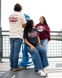 Three friends wearing Dr. Pepper merchandise pose together on a pier, with a scenic waterfront visible in the background.