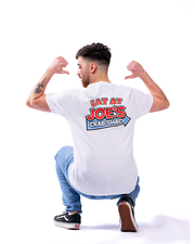 A person from behind, crouching and flexing muscles, wearing a white t-shirt with the slogan ‘EAT AT JOE’S CRAB SHACK’ in red and blue, paired with blue jeans and black sneakers, set against a white background.